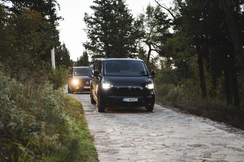 Two black Monte Zeta vans driving down a stone road between the trees