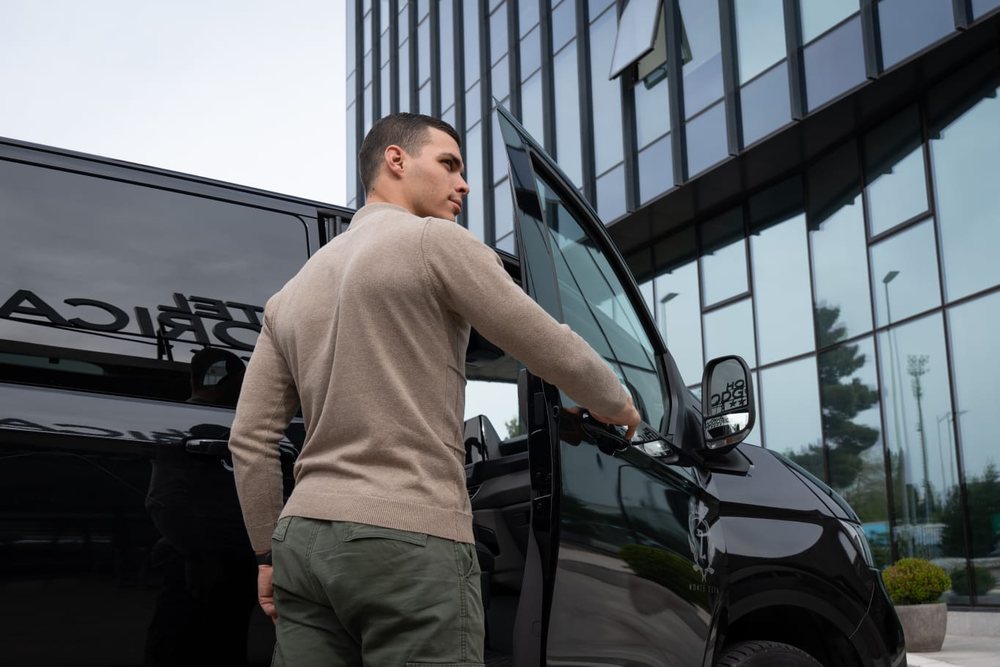 Monte Zeta chauffeur opening the passenger door of a black van outside a glass office building in Podgorica