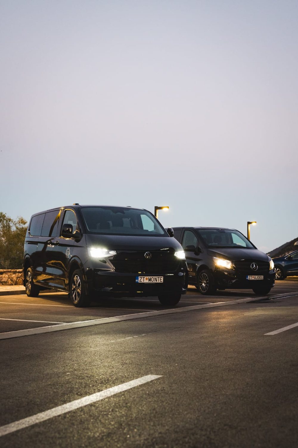 Two black Monte Zeta vans parked at dusk with their headlights on