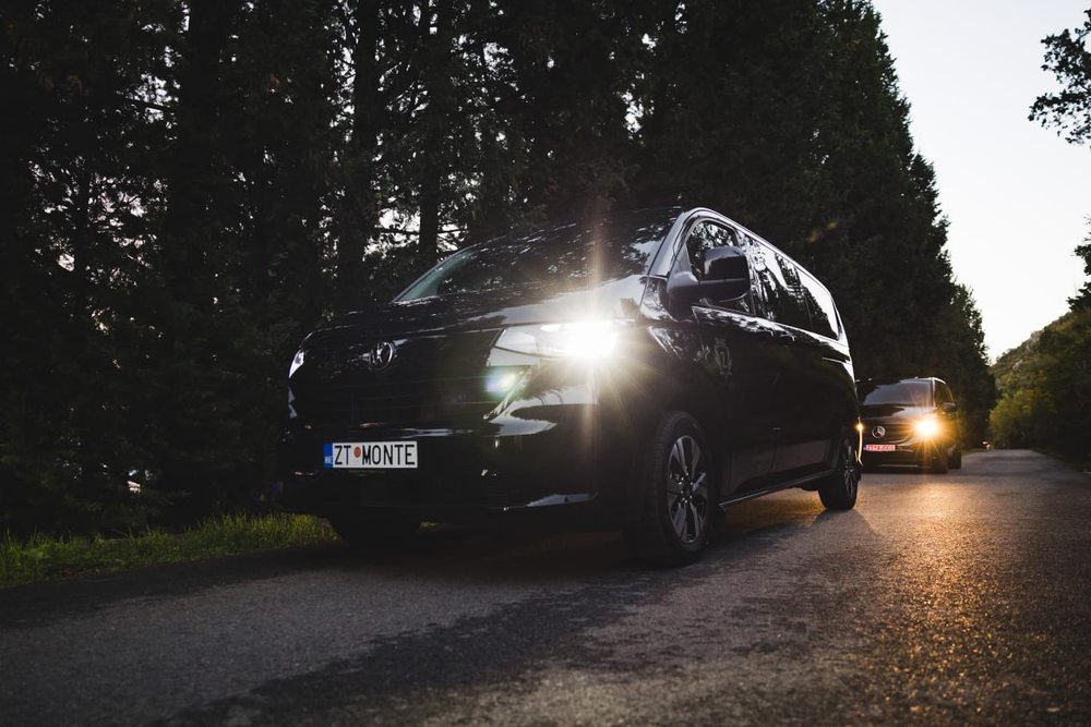 Black Volkswagen Multivan with its headlights on, on a forest road in Montenegro