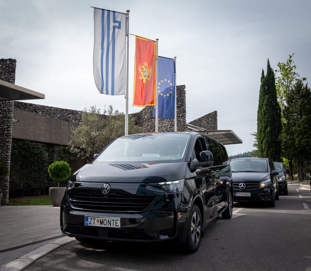 Three Monte Zeta vehicles lined up in front of a resort with Montenegrin and EU flags