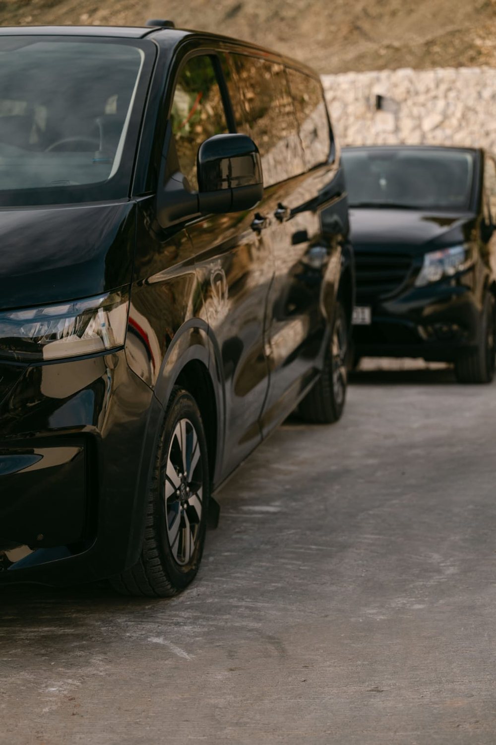 Two black vans of the Monte Zeta fleet parked side by side beside a stone wall